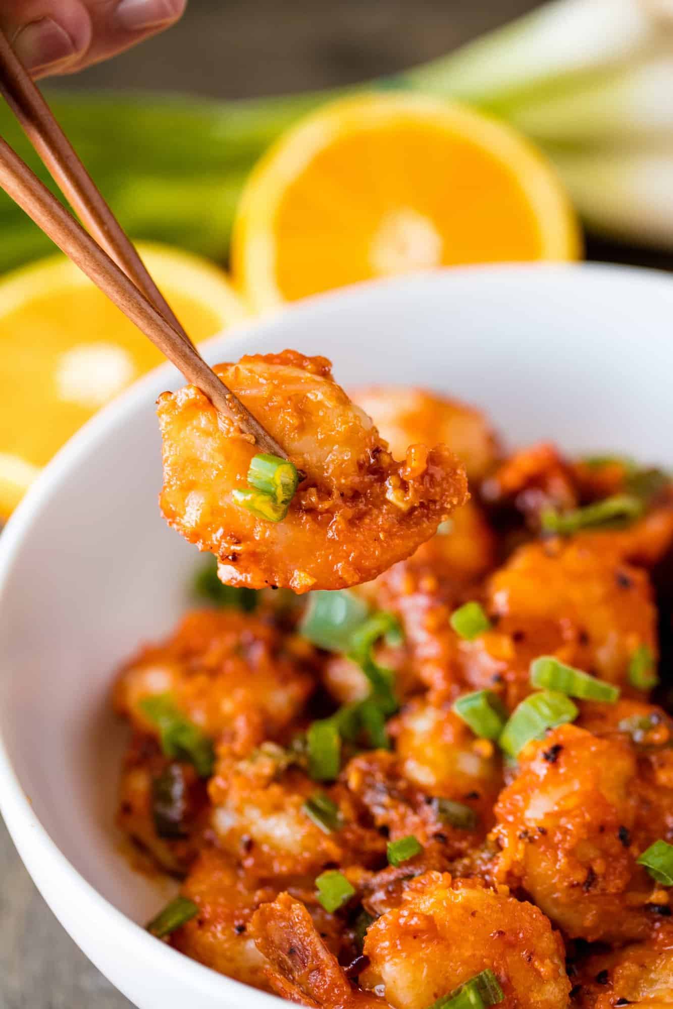 A bite of orange peel shrimp is lifted from a bowl with a pair of chopsticks
