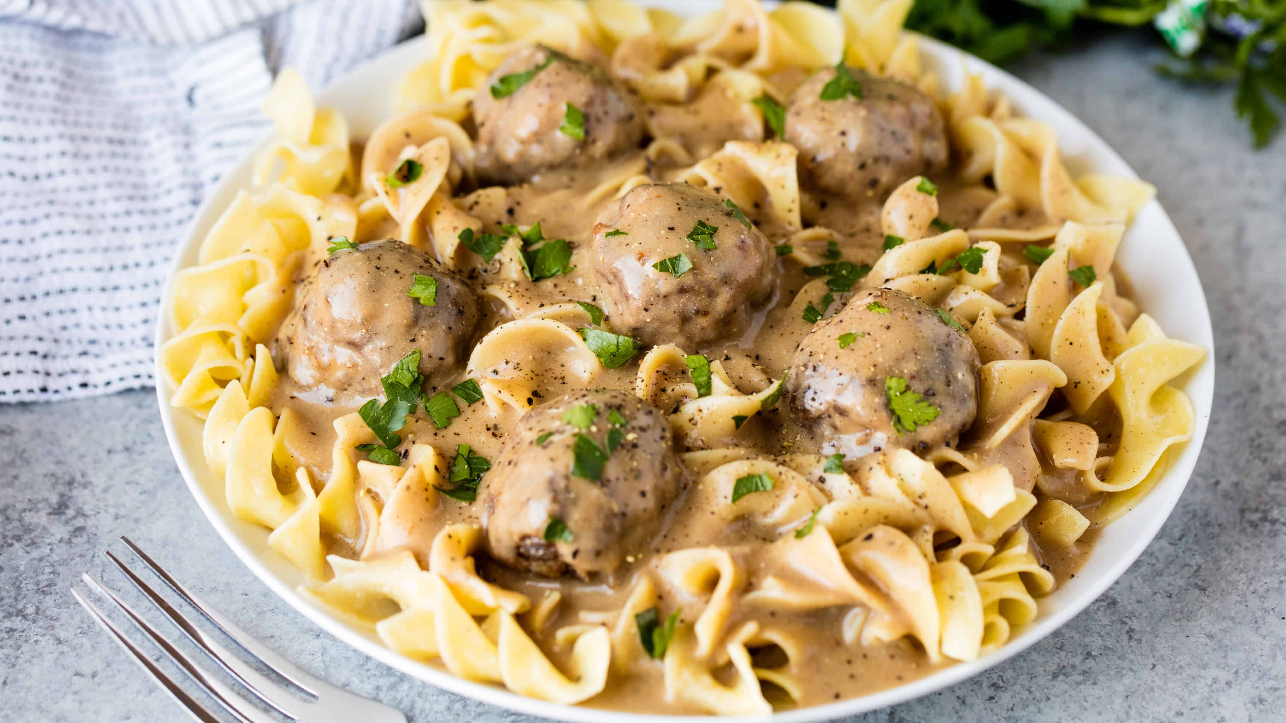 Swedish meatballs and gravy over egg noodles on a white plate.
