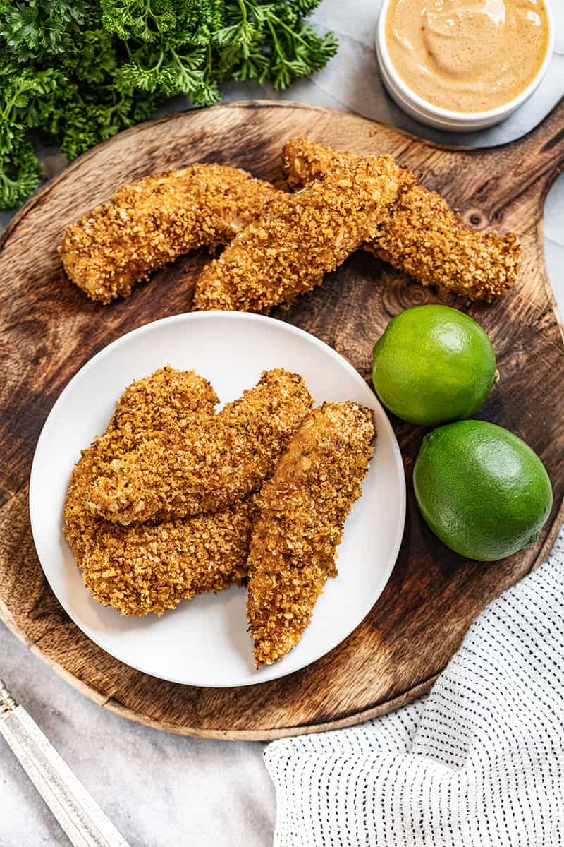 4 chicken tender strips on a white plate with limes