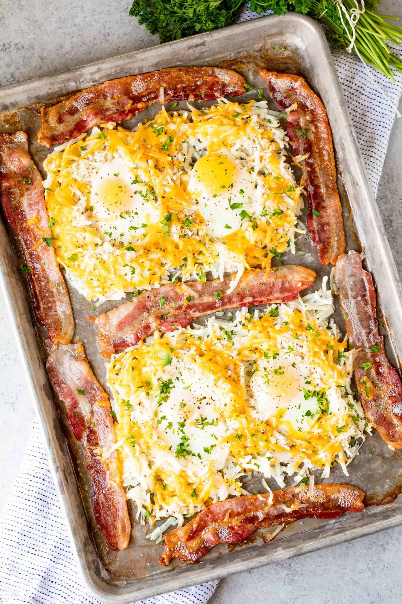 Crispy bacon surrounds eggs cooked in nests of hash browns on a sheet pan