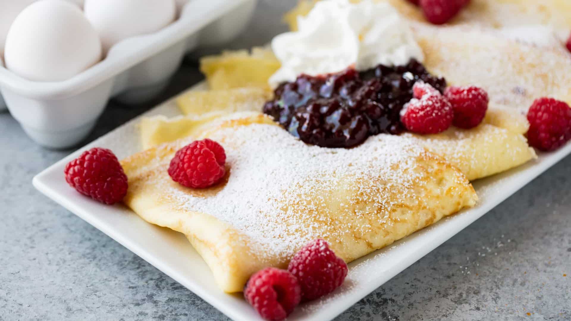Fluffy Swedish Pancakes on a white plate. Topped with berries and powdered sugar.