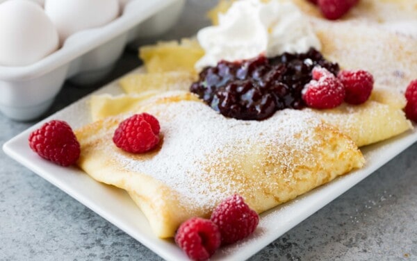 Fluffy Swedish Pancakes on a white plate. Topped with berries and powdered sugar.