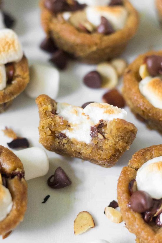 Rocky road cookie cups filled with marshmallows, slivered almonds and chocolate chips, one with a bite taken out