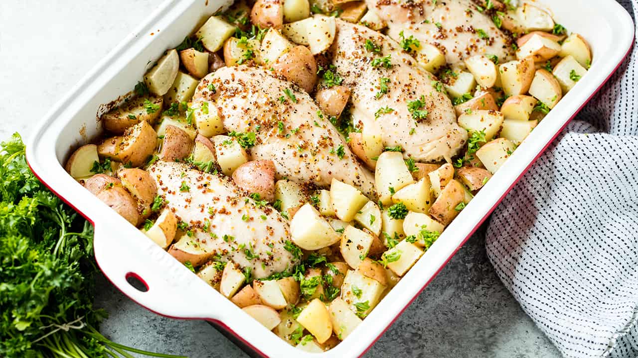 Angled view of Baked Honey Dijon Chicken and Potatoes garnished with parsley, in a casserole dish on a concrete countertop.