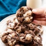 Chocolate Marshmallow Chubbie being held by a hand over a plate of Chocolate Marshmallow Chubbies.