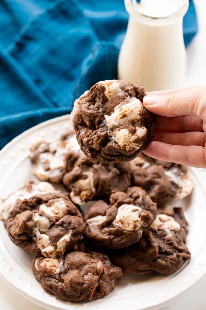 Chocolate Marshmallow Chubbie being held by a hand over a plate of Chocolate Marshmallow Chubbies.