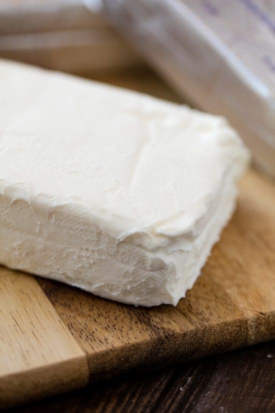 Close up of a block of cream cheese on a cutting board.