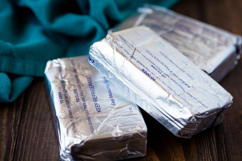 Three wrapped cream cheese blocks on a wood countertop.