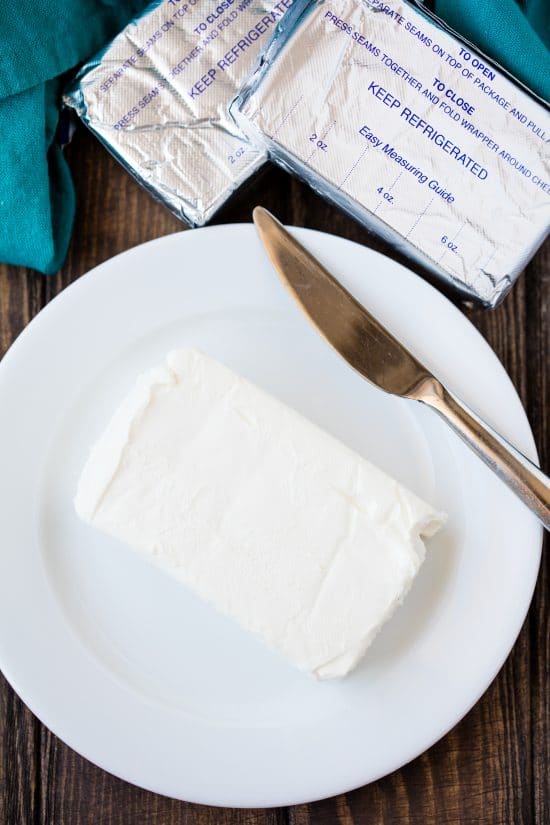 A block of cream cheese on a white plate with a knife on it.