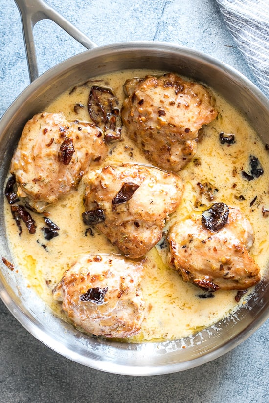 Creamy sun-dried tomato chicken sitting in sauce in a stainless steel pan.