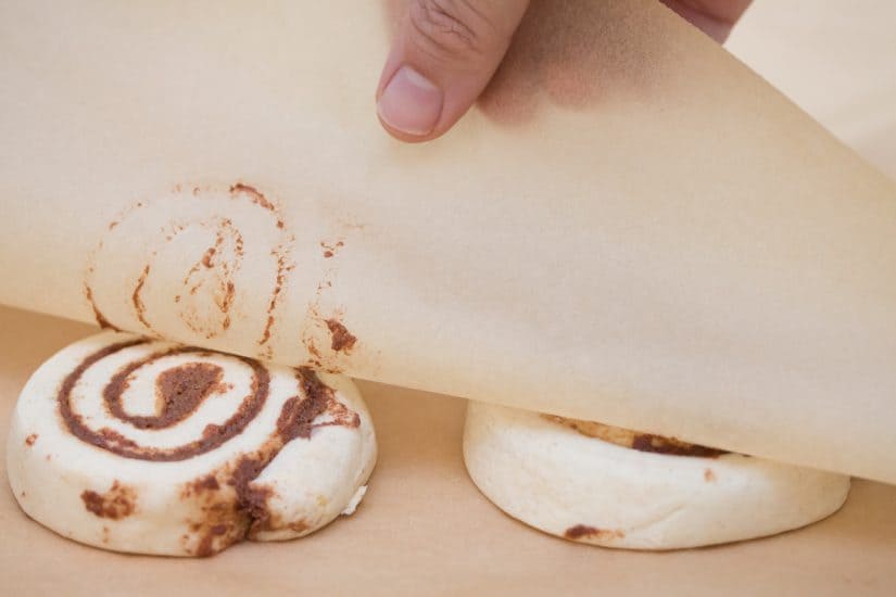 Cinnamon roll dough in between two pieces of parchment paper getting squished down to be flat.