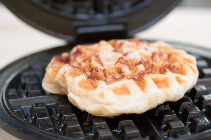 Cinnamon roll dough being cooked in a waffle iron.