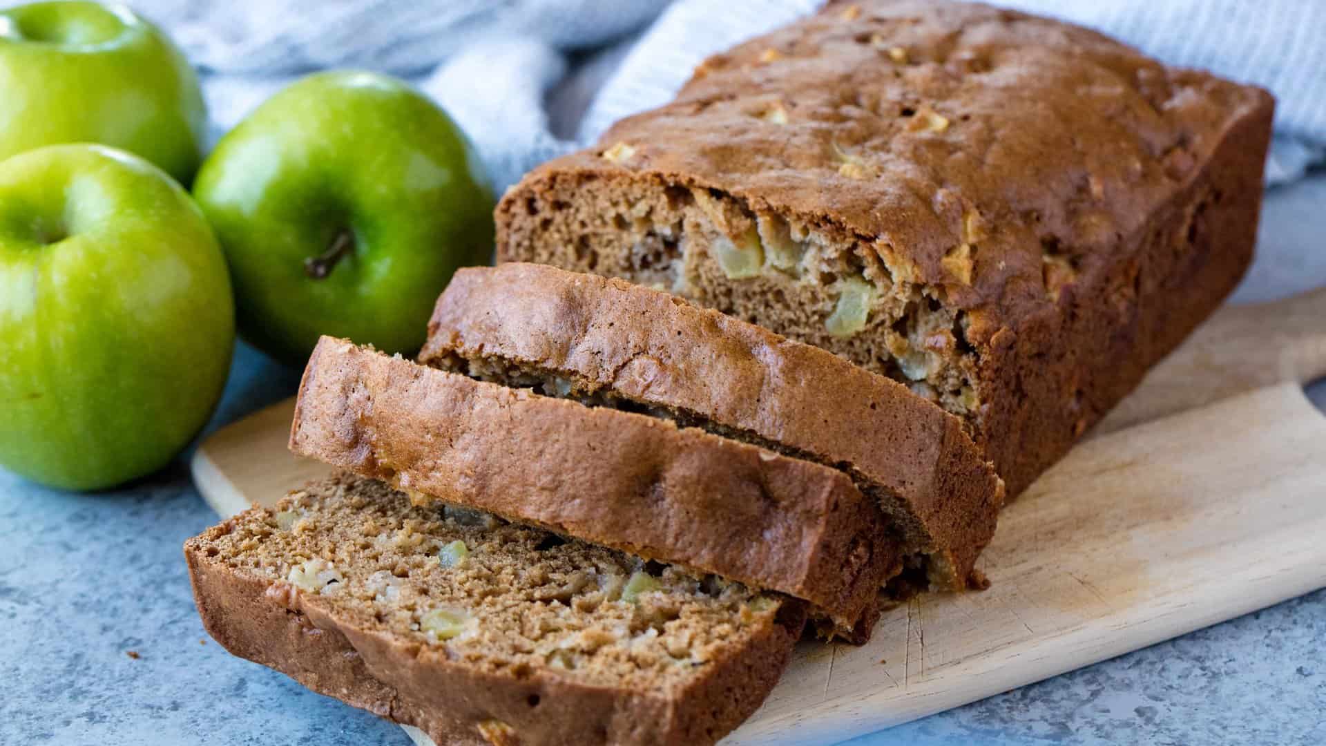 Sliced loaf of apple bread with granny smith apples in the background
