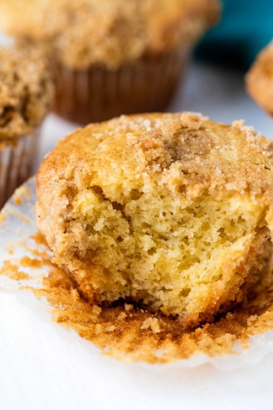 Close up of a sour cream coffee cake muffin with its wrapper half off and a bite taken out of it.