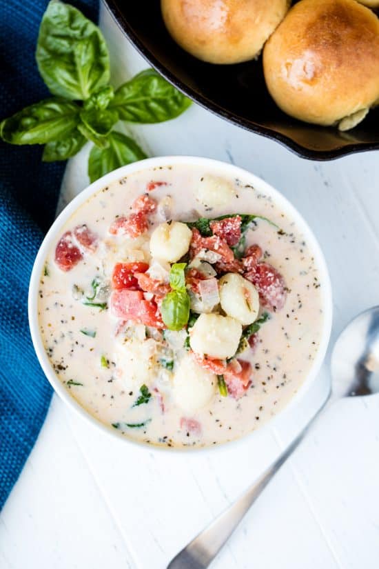 A bowl of Creamy Spinach Tomato Gnocchi Soup garnished with fresh basil and served with skillet rolls