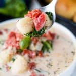 A spoon lifts a bite of Creamy Spinach Tomato Gnocchi Soup with gnocchi, spinach and tomato