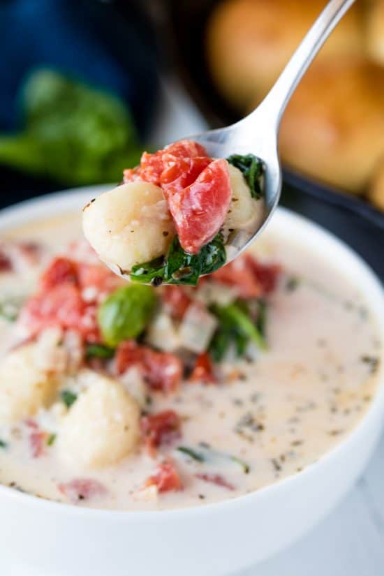 A spoon lifts a bite of Creamy Spinach Tomato Gnocchi Soup with gnocchi, spinach and tomato