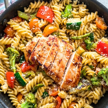 Pasta with broccoli, bell pepper, cherry tomatoes and zucchini topped with a sliced chicken breast in a skillet