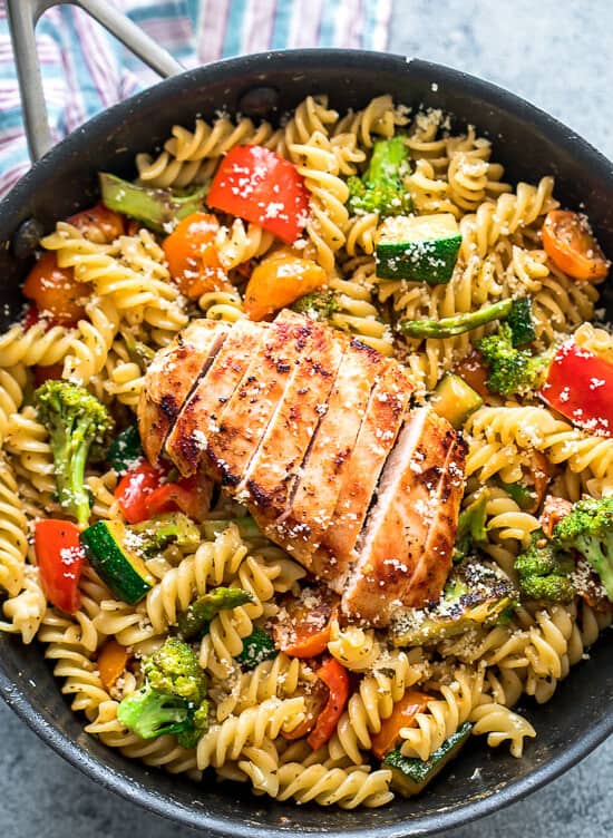 Pasta with broccoli, bell pepper, cherry tomatoes and zucchini topped with a sliced chicken breast in a skillet