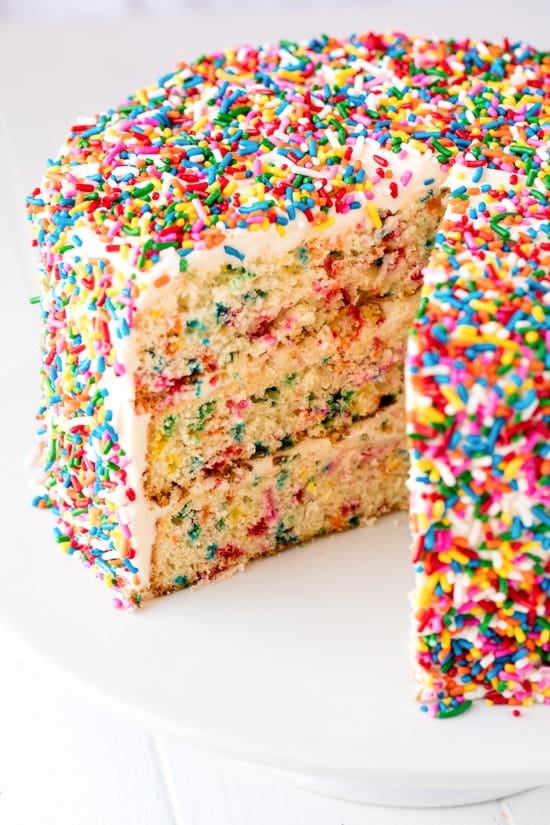 Funfetti Birthday Cake with a slice missing on a white cake stand.