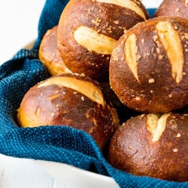 Homemade pretzel rolls in a basket with a blue towel