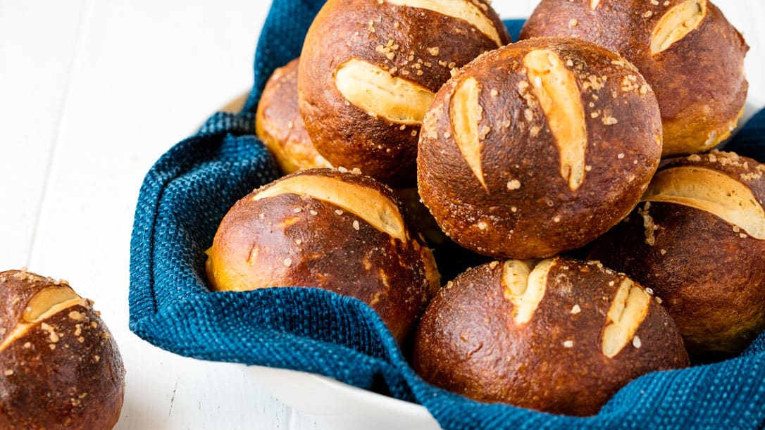 Homemade pretzel rolls in a basket with a blue towel