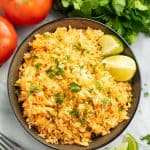 Bird's eye view of Mexican rice and two lime wedges in a black bowl.