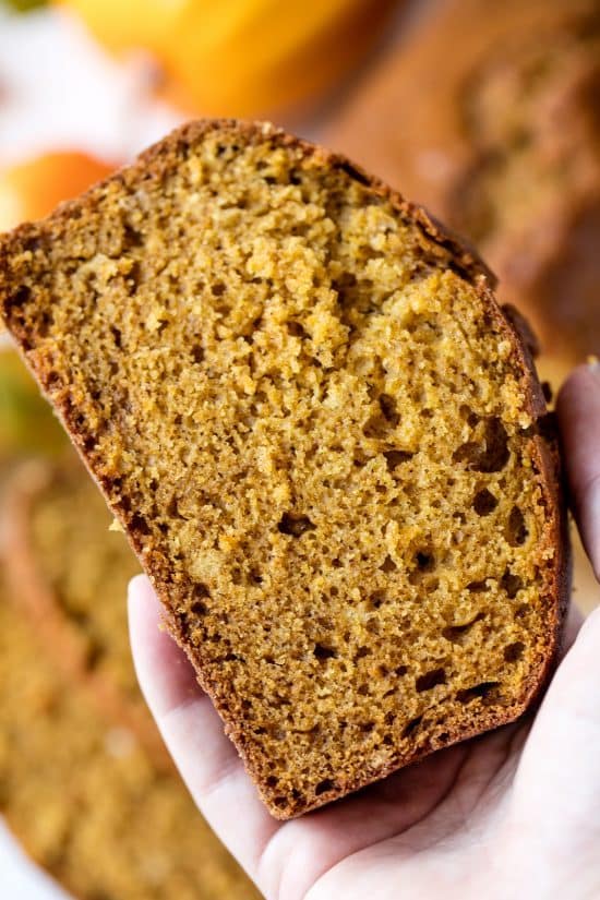 A hand is holding a slice of pumpkin bread. 