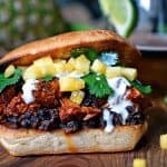 Close up of a Pineapple Chile Pulled Pork Sandwiches sitting on a wood counter top with a drink in the background.