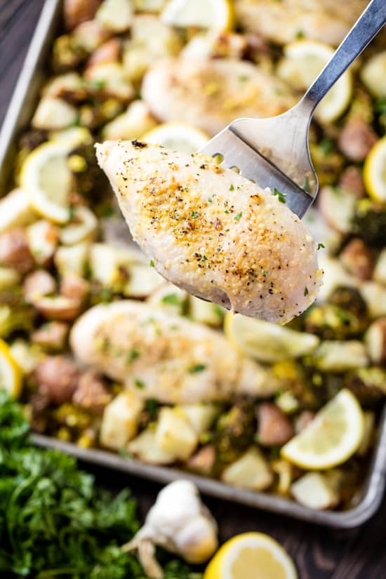 Spatula holding chicken breast over a Sheet Pan Garlic Parmesan Chicken Broccoli and Potatoes. 