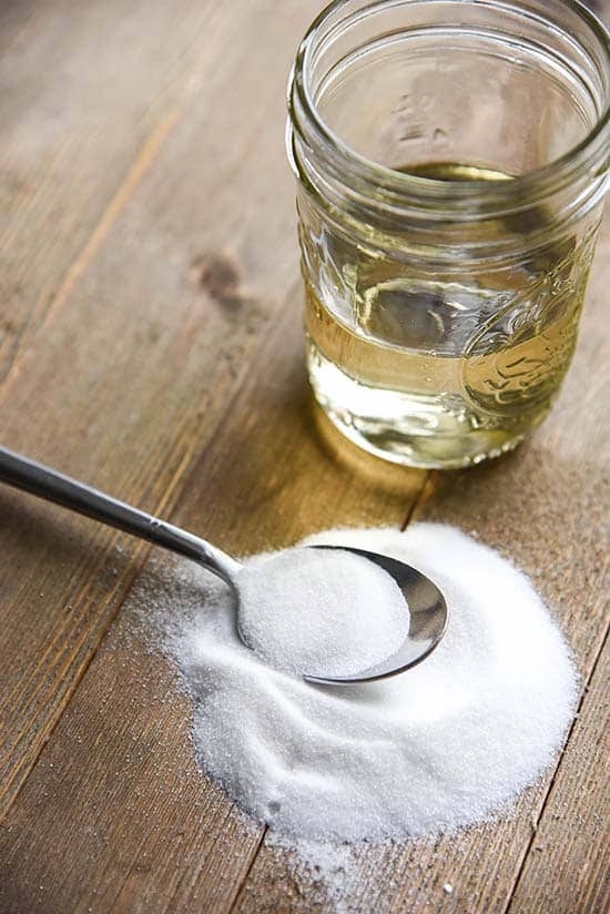 Wood countertop with a spoon laying in a sugar pill with a jar full of homemade water syrup in the background.