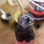 Blueberry Lemonade in a small glass half-filled with blueberries with a straw in it.