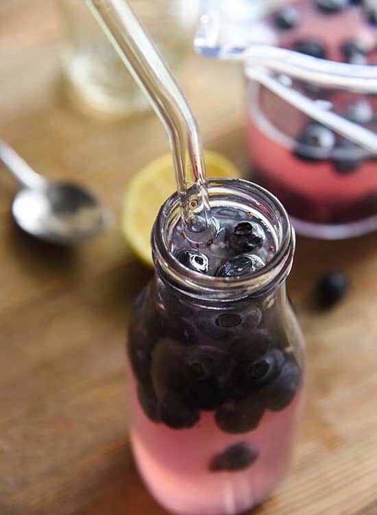 Blueberry Lemonade in a small glass half-filled with blueberries with a straw in it.