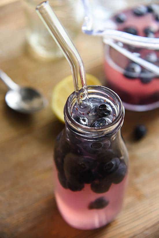 Blueberry Lemonade in a small glass half-filled with blueberries with a straw in it.