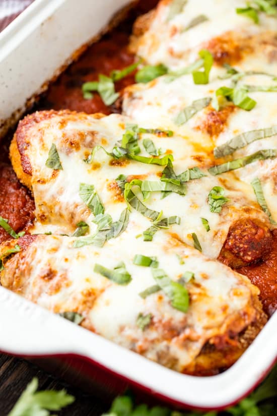 Baked chicken parmesan in a red pan with basil on it.