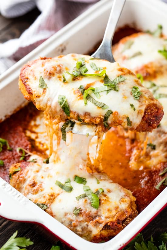 Baked Chicken Parmesan being lifted out of the pan with a silver spatula.
