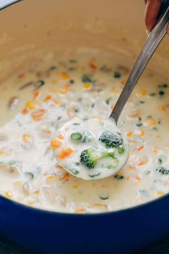 A ladle of Creamy Vegetable Soup with broccoli, carrots, celery, corn and mushrooms, taken from the pot