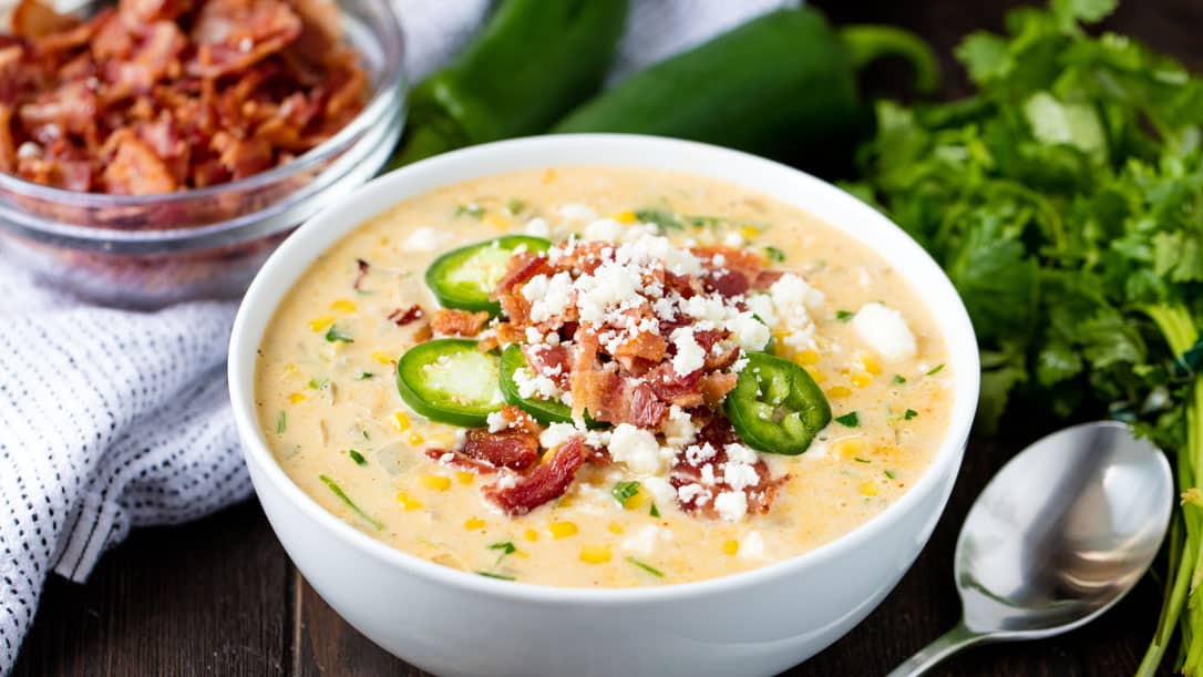 Mexican street corn soup in a white bowl garnished with bacon, jalapenos, and cotija cheese