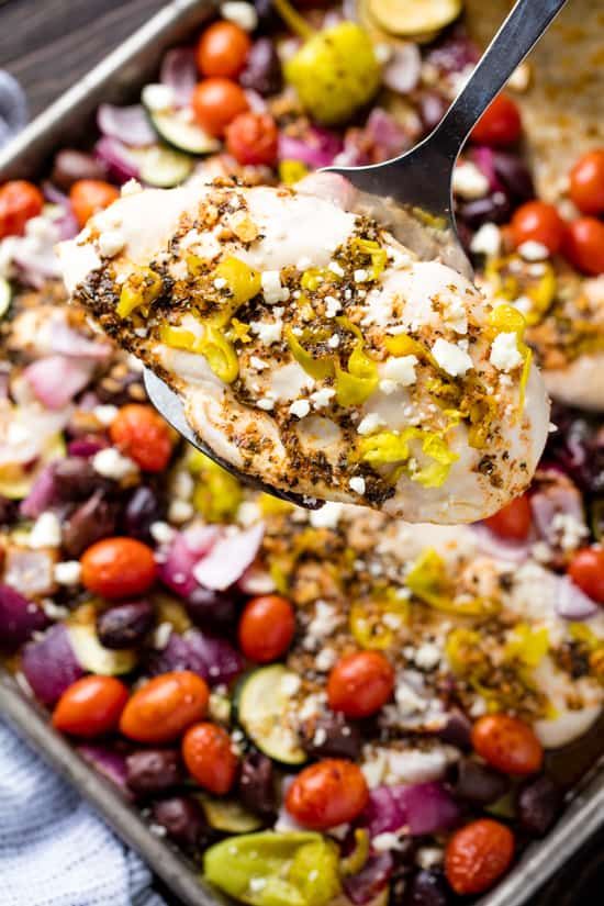 Greek Chicken with slices of pepperoncini and crumbled feta cheese taken from a pan of Sheet Pan Greek Chicken and Veggie Bake