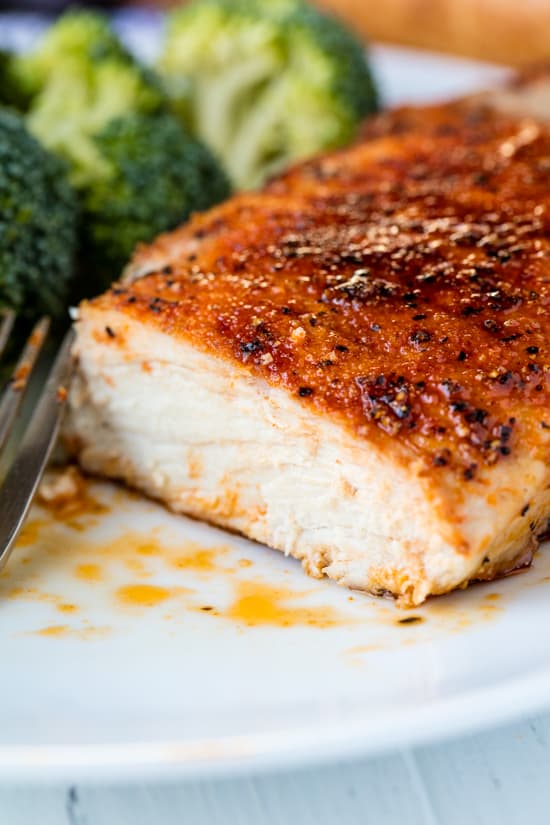 A juicy, baked pork chop sliced into on a plate with a side of broccoli