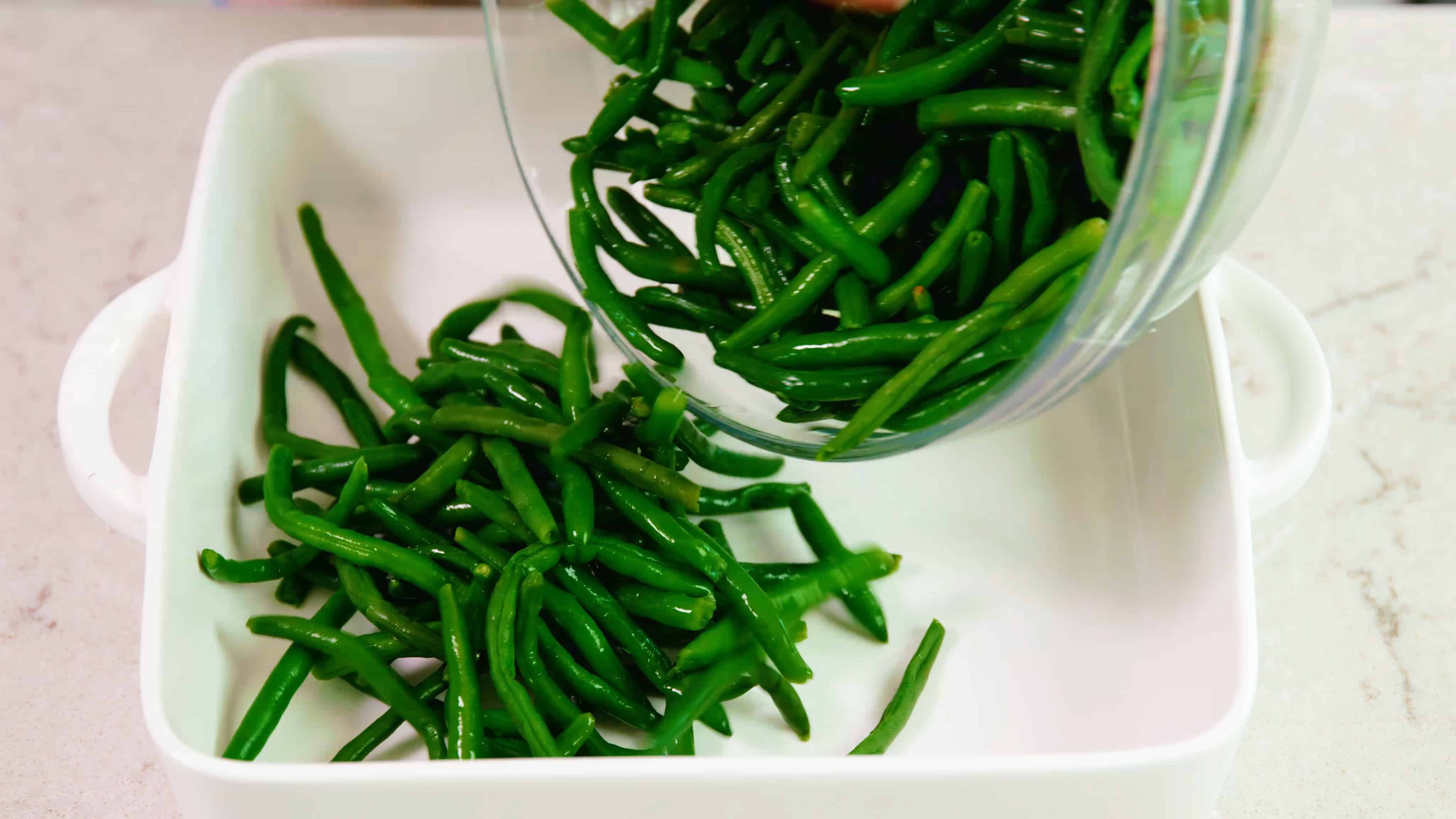 Green beans getting poured into a baking dish.