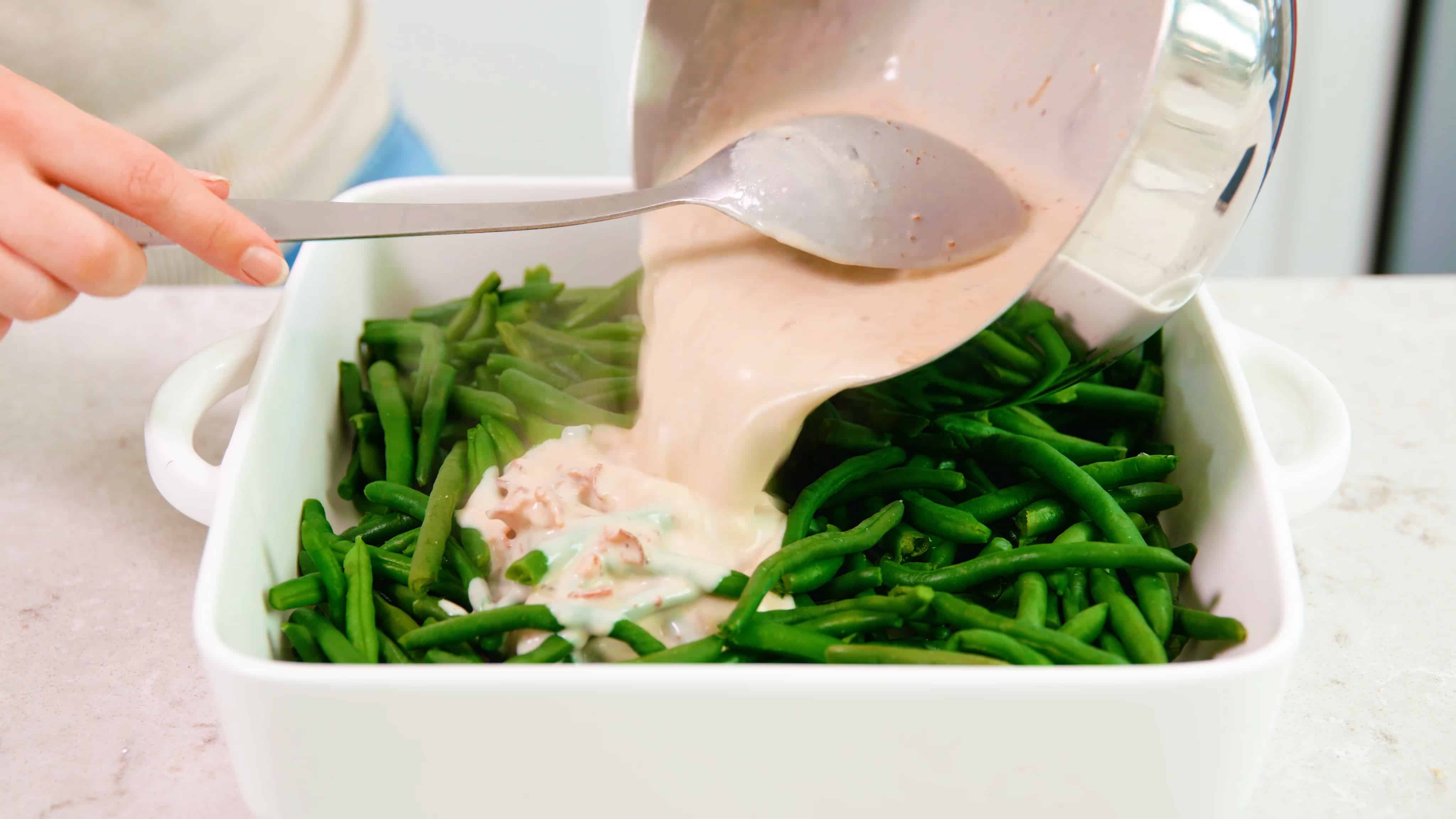 Green beans in a baking dish getting sauce poured on them.