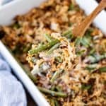 Green Bean Casserole on a wooden spoon above a dish full of green bean casserole.