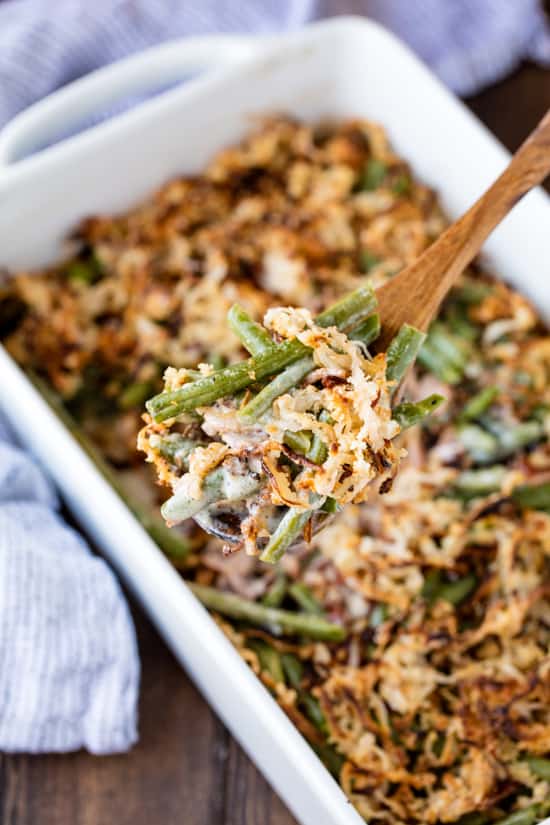 Green Bean Casserole on a wooden spoon above a dish full of green bean casserole.