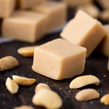 Pieces of peanut butter fudge stacked on a counter with peanut halves scattered around them