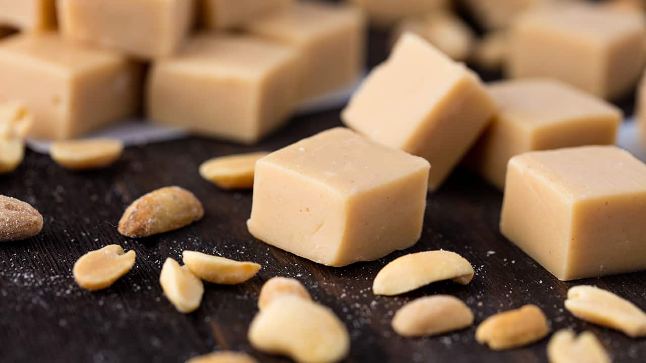 Pieces of peanut butter fudge stacked on a counter with peanut halves scattered around them