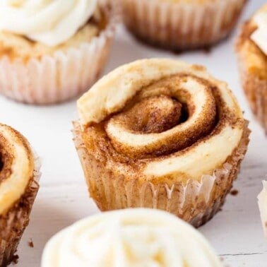 Several cinnamon roll cupcakes on a marble slab topped with cream cheese frosting