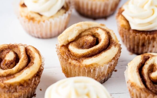Several cinnamon roll cupcakes on a marble slab topped with cream cheese frosting