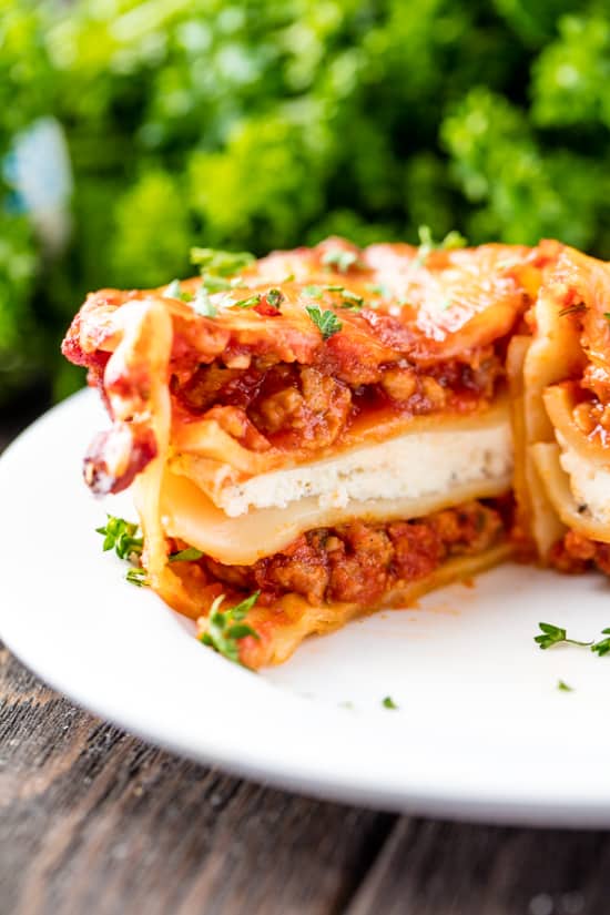 A Mini Lasagna Cup cut in half, layered with cheese, sausage, sauce and noodles, topped with chopped fresh parsley