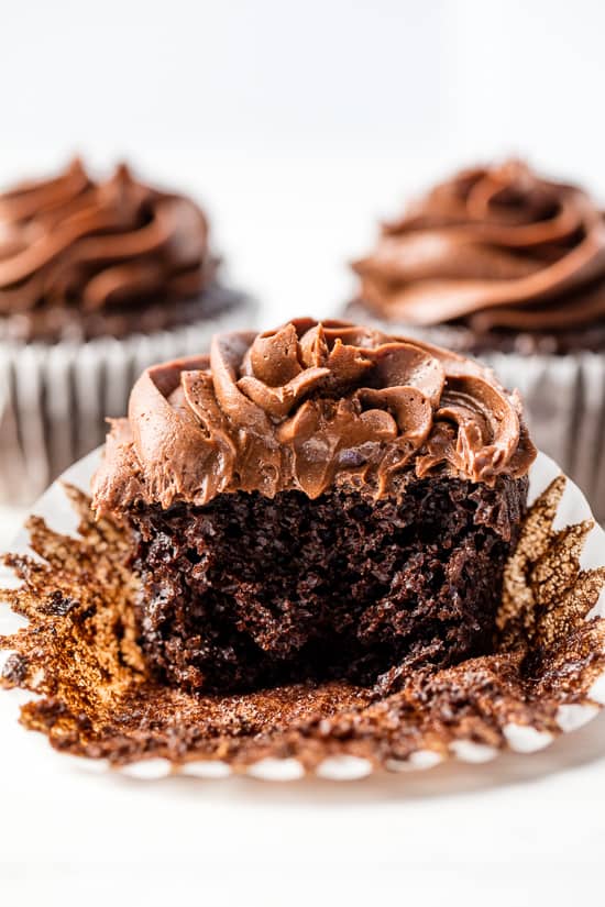 A moist chocolate cupcake with chocolate frosting with a bite taken out of it